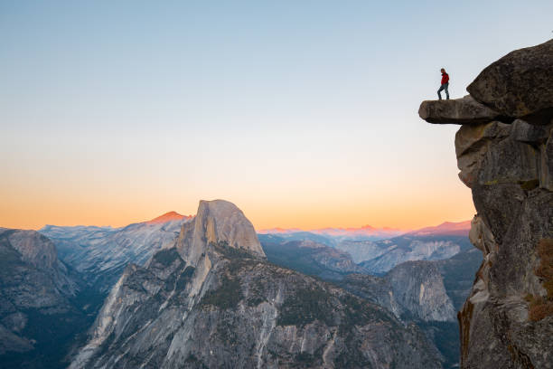Hiker in Yosemite National Park, California, USA A fearless hiker is standing on an overhanging rock enjoying the view towards famous Half Dome at Glacier Point overlook in beautiful evening twilight, Yosemite National Park, California, USA wilderness stock pictures, royalty-free photos & images