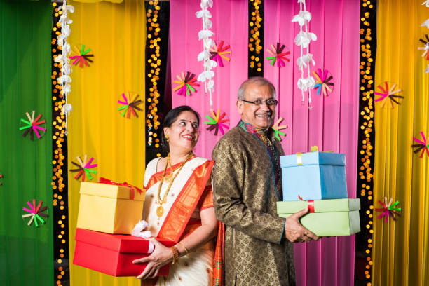 istock Senior Indian couple holding Diwali Gift Boxes while standing against decorative background 1135114931