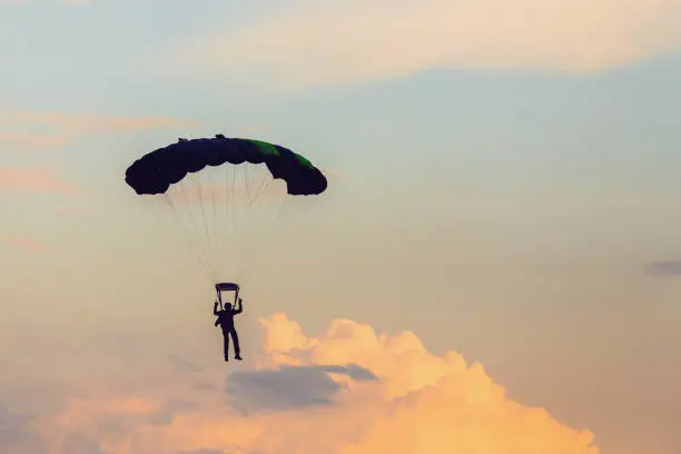 Parachutist falling from the sky in evening sunset dramatic sky. Recreational sport, Paratrooper silhouette on colored sky.