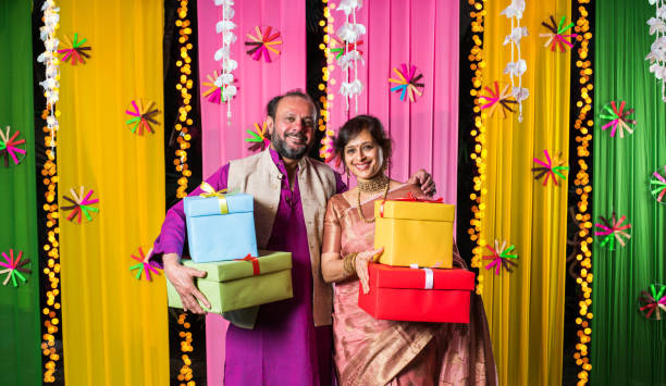 istock Mid age Indian couple holding Diwali Gift Boxes while standing against decorative background 1135116185