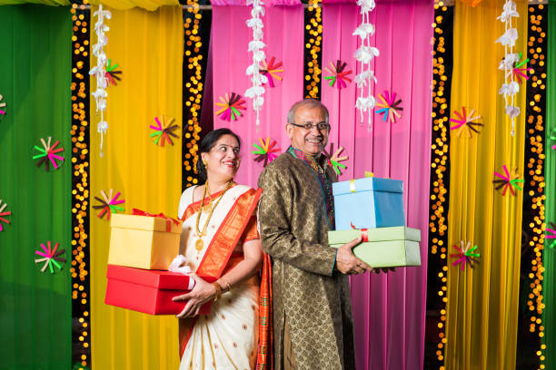 istock Senior Indian couple holding Diwali Gift Boxes while standing against decorative background 1135116327