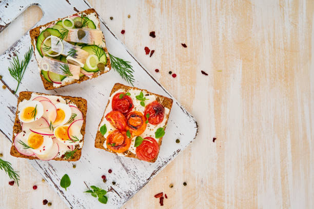 istock Smorrebrod - traditional Danish sandwiches. Black rye bread with herring, egg, tomatoes, radish on white wooden table, top view 1135117668