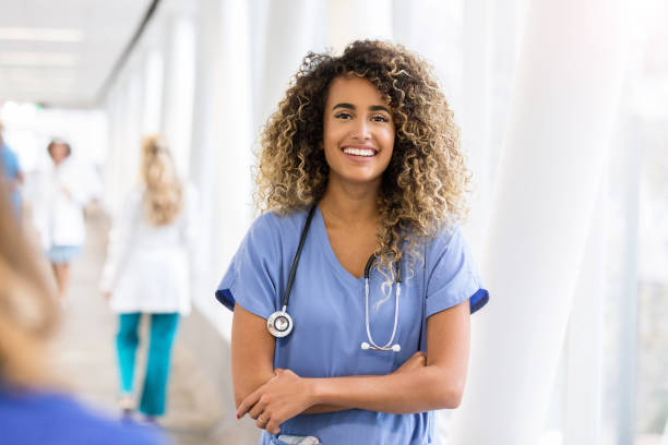 Young female nurse smiles for camera in elevated walkway A smiling young female nurse stands in a busy elevated walkway and smiles for the camera with her arms folded.  She is wearing scrubs and a stethoscope. elevated walkway photos stock pictures, royalty-free photos & images