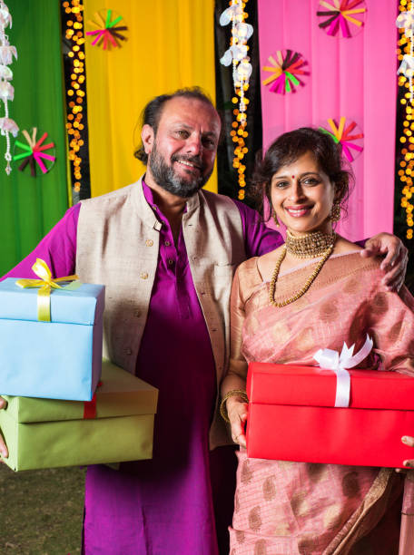 istock Mid age Indian couple holding Diwali Gift Boxes while standing against decorative background 1135118379