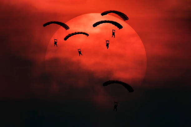 Five parachutes silhouette in front of big sun with smoke in battle field mood