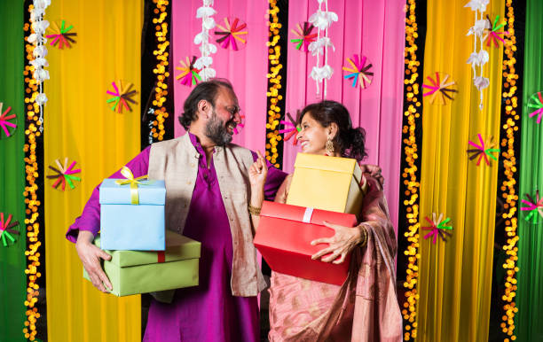 istock Mid age Indian couple holding Diwali Gift Boxes while standing against decorative background 1135119500