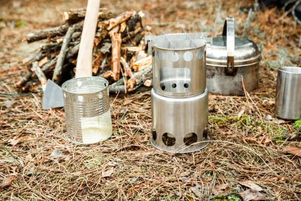 camping woodstove and utensils, axe near a firewoods, and backpack on the background