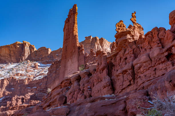 Wide view of the dramatic sandstone spires of Fisher Towers rising above the desert landscape near Moab, Utah, with deep shadows, layered rock formations, and a vast open sky in the American Southwest.