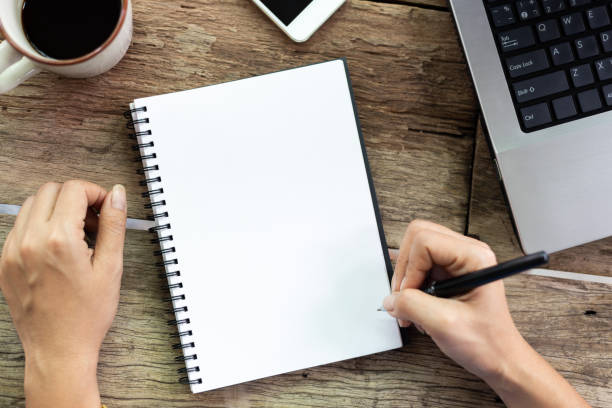 istock Top view Female hand is writing blank paper and computer on old wooden table 1135133225