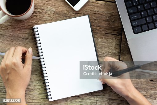istock Top view Female hand is writing blank paper and computer on old wooden table 1135133225