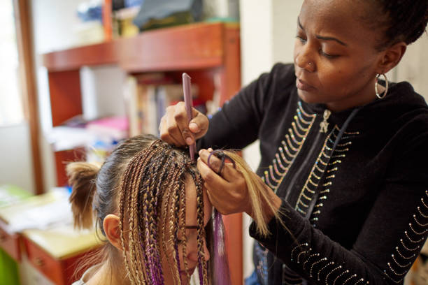 African Woman Styling Friend's Hair African woman making braids to her friend. black woman hair extensions stock pictures, royalty-free photos & images