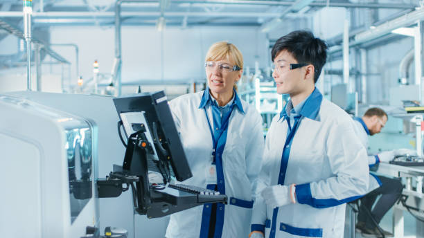 en la fábrica de alta tecnología asia ingeniero habla con el supervisor femenino, utilice la computadora para la selección de la programación y coloque la maquinaria electrónica para la línea de montaje de montaje superficial de la placa de circuito  - technology computer chip industry electrical equipment fotografías e imágenes de stock