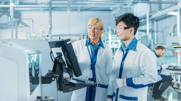 ハイテク工場でアジアのエンジニアは、女性のスーパーバイザーと話をします, プログラミングのためのコンピュータを使用してくださいプリント基板表面実装組立ライン用のピックアンド� - pharmaceutical factory healthcare and medicine industry laboratory ストックフォトと画像