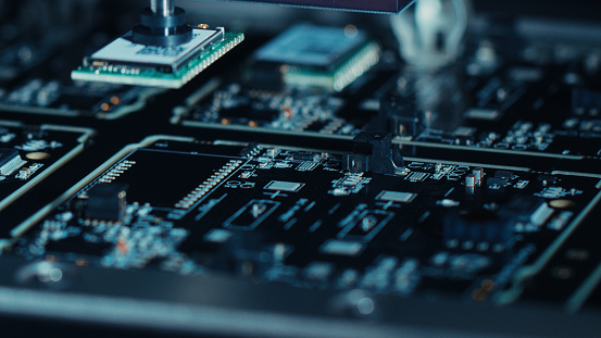 Close-up Macro Shot of Electronic Factory Machine at Work: Printed Circuit Board (PCB) Being Assembled with Automated Robotic Arm, Surface Mounted Technology (SMT) Connecting Microchips to Motherboard.