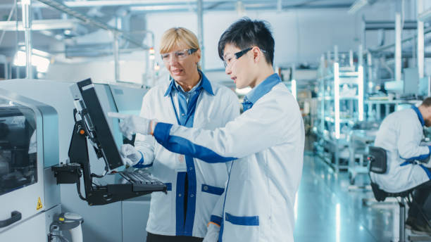 On High-Tech Factory Asian Engineer Talks with Female Supervisor, Use Computer for Programming Pick and Place Electronic Machinery for Printed Circuit Board Surface Mount Assembly Line. Production of PCB with SMT Machinery. en la fábrica de alta tecnología asia ingeniero habla con el supervisor femenino, utilice la computadora para la selección de la programación y coloque la maquinaria electrónica para la línea de montaje de montaje superficial de la placa de circuito