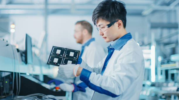 istock High-Tech Factory: Quality Control Engineer Checks Electronic Printed Circuit Board it for Damages. In the Background Assembly Line for PCB with Surface Mount Pick and Place Technology. 1135140601