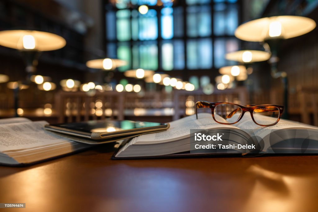 Digital Tablet and Eyeglasses On Books in Public Library Book Stock Photo