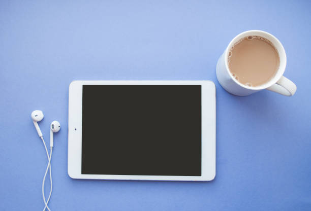 Flat lay of white tablet, earphones and a cup of coffee on purple background with copyspace.