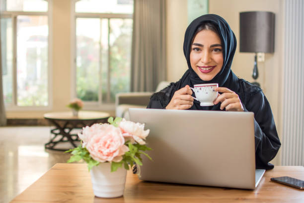 istock Young Arab woman with coffee cup using laptop and looking at camera 1135150967