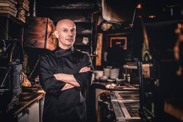 Confident chef posing with his arms crossed and looking at a camera in restaurant kitchen.