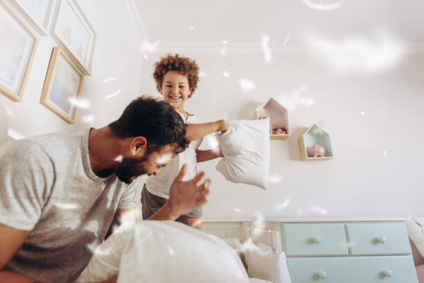 padre e hijo divirtiéndose jugando en casa - lucha con almohada fotografías e imágenes de stock