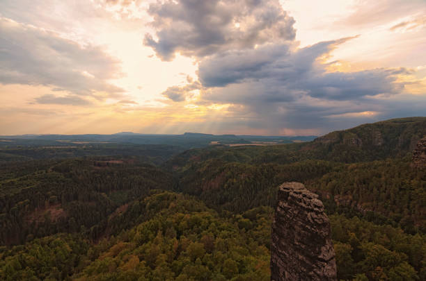Panorama with typical rocky peaks under thunderstorms clouds. The sun's rays make their way through dense clouds. Bohemian Switzerland National Park. Czech Republic.