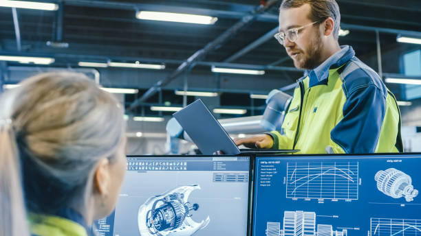 istock At the Factory: Male and Female Mechanical Engineers Use Laptop and Personal Computer while Discussing Robotic Arm Manufacturing Project. Screen Shows 3D Engine Concept made with CAD Software. 1135159512