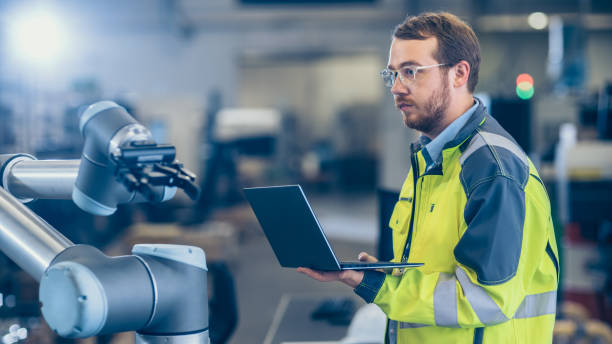 istock At the Factory: Automation Engineer Uses Laptop for Programming Robotic Arm. New Era in Automatic Manufacturing Industry. 1135159519