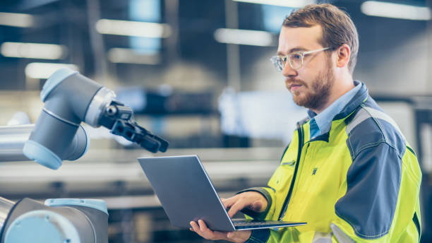 istock At the Factory: Automation Engineer Uses Laptop for Programming Robotic Arm. New Era in Automatic Manufacturing Industry. 1135159534