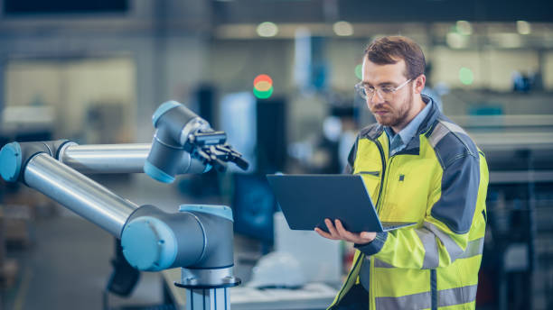 istock At the Factory: Automation Engineer Uses Laptop for Programming Robotic Arm. New Era in Automatic Manufacturing Industry. 1135159542