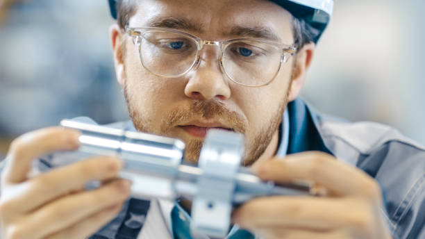 Close-up Shot of the Industrial Engineer Wearing Classes and Hard Hat Connects Two Components He Designed. Precision in Mechanical Engineering. Close-up Shot of the Industrial Engineer Wearing Classes and Hard Hat Connects Two Components He Designed. Precision in Mechanical Engineering. metal industry stock pictures, royalty-free photos & images