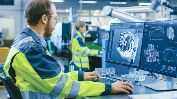 istock At the Factory: Mechanical Engineer Works on Computer, Designs in CAD 3D Model of the Engine. In the Background Factory Workers and Manufacturing Process. 1135159658