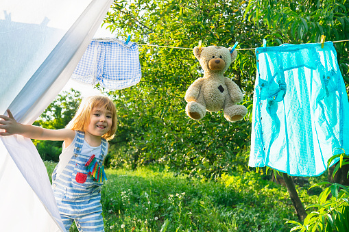 Cute blond boy looking through laundry in the garden.