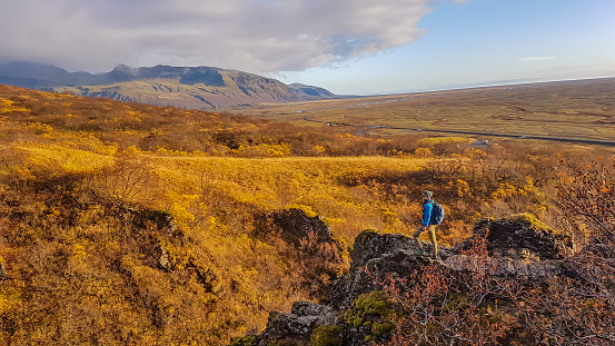 A man standing on  top of a hill. Autumn vibes seen from a top of a mountain. Grass and bushes turned gold. Bright sun makes them shine. In the back a volcano and higher mountain ranges.