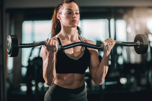 istock Attractive Caucasian female bodybuilder with ponytail lifting barbell while standing in gym. Think big and results will come. 1135163868