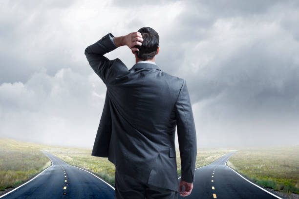 istock Businessman Standing At Fork In Road Looking Into The Distance 1135168159