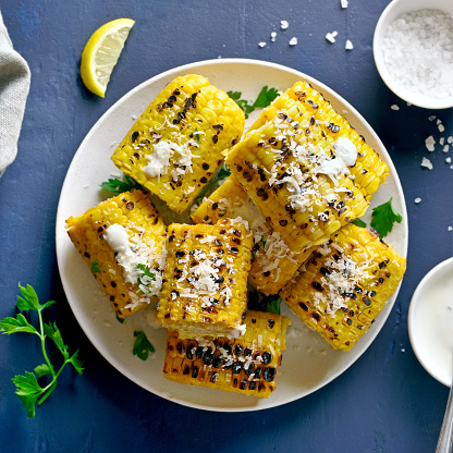 Grilled corn on the cob with sauce and parmesan over blue stone background. Top view, flat lay