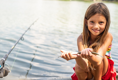 Cute little girl showing two small fish at the river bank