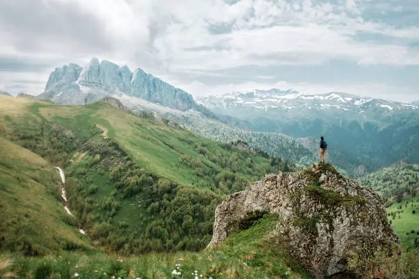 Female traveler standing on cliff and looking at rocky mountain.