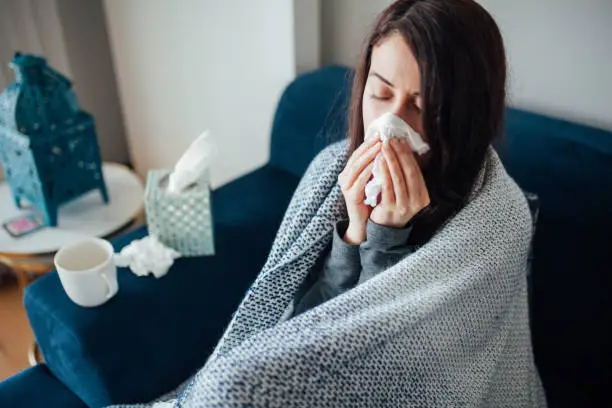 Sick woman blowing her nose, she covered with blanket