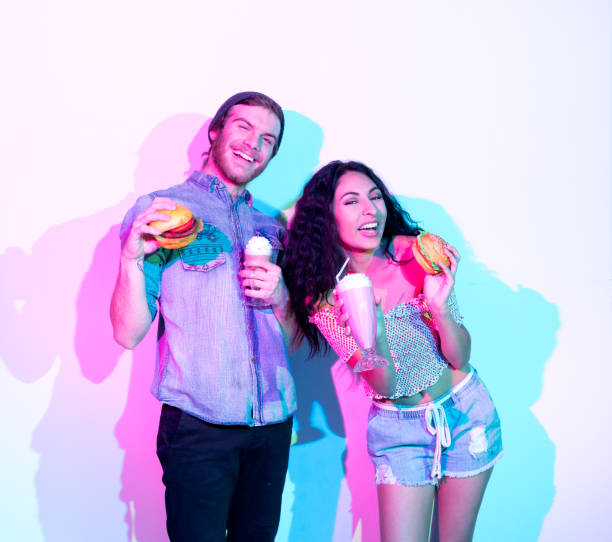 흰 벽 앞에 서 있는 매력적인 남자와 여자 - unhealthy eating flash 뉴스 사진 이미지