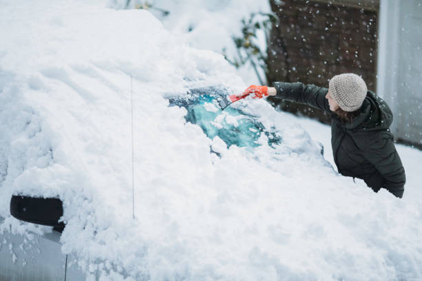 Woman Scraping Snow and Ice off Car Windshield A Caucasian adult woman cleans the snow and ice from the windshield of her minivan. scraping stock pictures, royalty-free photos & images