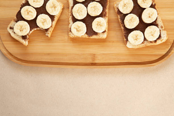 istock Three banana white bread toasts smeared with chocolate butter that lie on a cutting board on craft paper background. top view with area for text 1135199052
