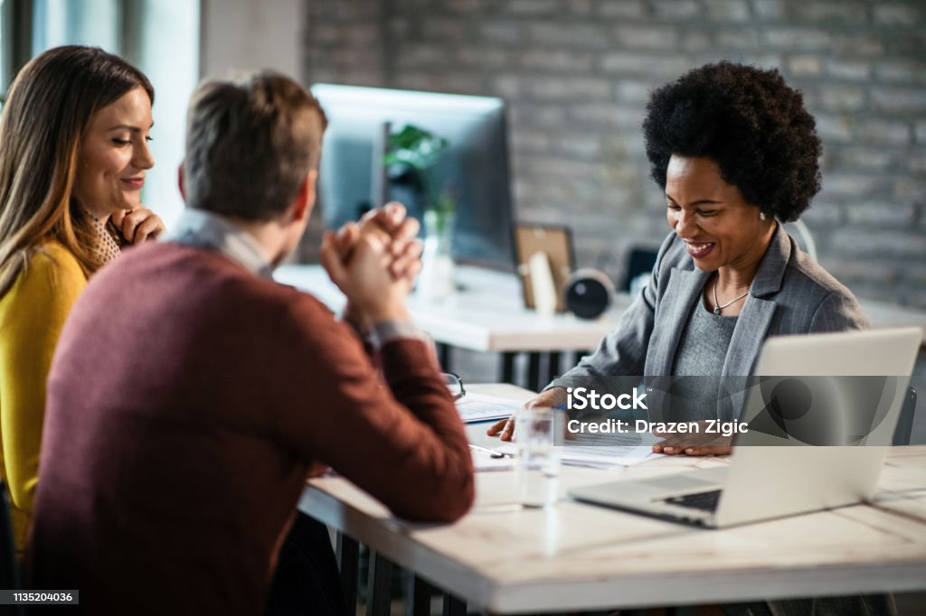 Cheerful African American financial advisor on a meeting with a couple. Happy African American insurance agent going through reports while having consultations with a couple during the meeting. Banking Stock Photo