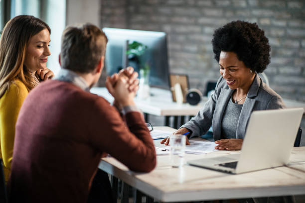 Cheerful African American financial advisor on a meeting with a couple. Happy African American insurance agent going through reports while having consultations with a couple during the meeting. african american business couple stock pictures, royalty-free photos & images