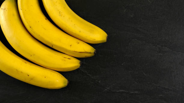 istock Top down view, four bananas on black slate board, space for text on right side. 1135211291