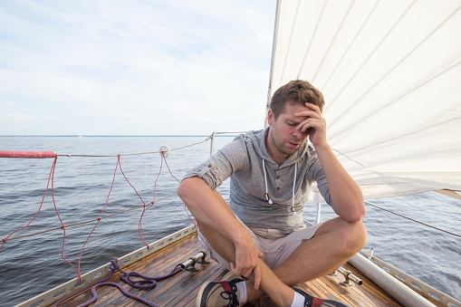 young european man having a nausea seasickness. He is trying to stop vomiting. Travelling on old boat with sail