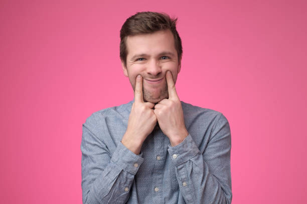 sad young man dressed in blue shirt makes faces trying to stay optimistic - bizarre making a face men one person imagens e fotografias de stock