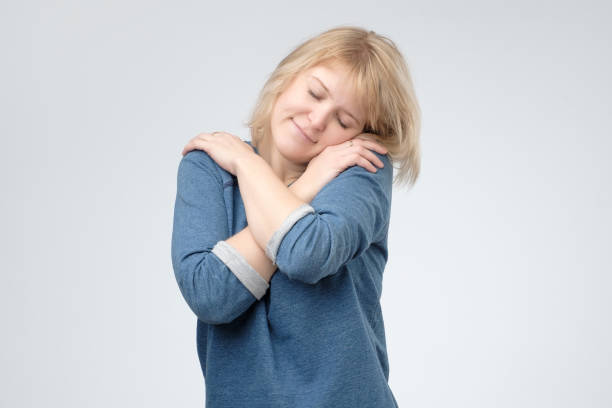 istock Charming female closing eyes in enjoyment, hugging herself, feeling comfortable and cozy 1135214989