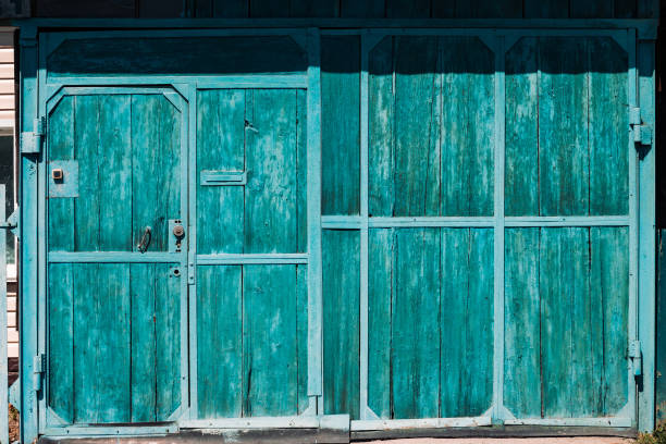 istock Closed rustic imperfect green garage gate with turquoise peeling paint close-up. Texture of locked wooden door with doorbell. Flaky dye on grungy wood planks. Rough faded wooden gates of village house 1135215507
